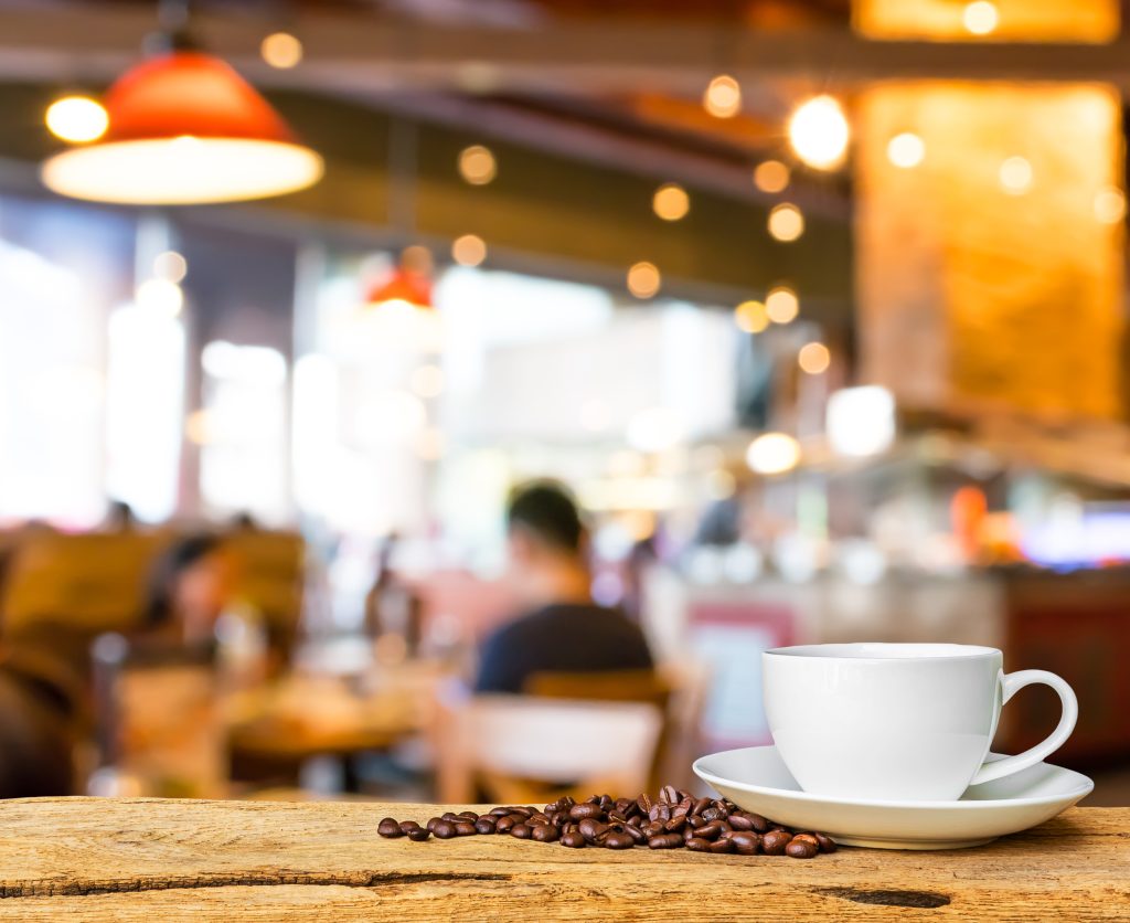 Mug with coffee beans next to it, a blurred coffee shop in the background