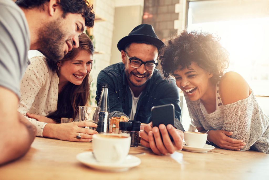 Portrait of cheerful young friends looking at smart phone while sitting in cafe.